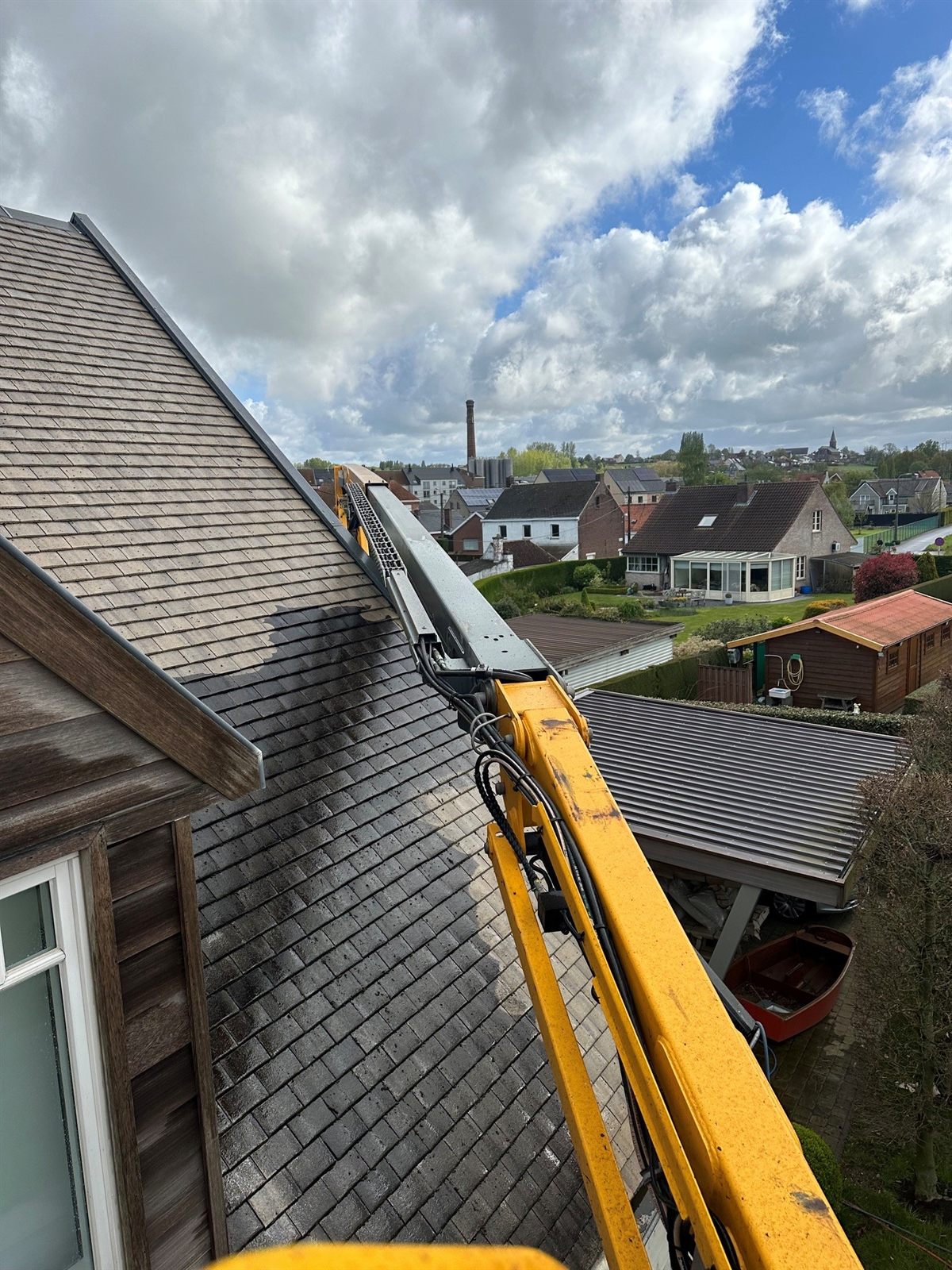 DTRenovatie-vakman reinigt met een hoogtewerker een dak, met zicht op de omliggende gemeente