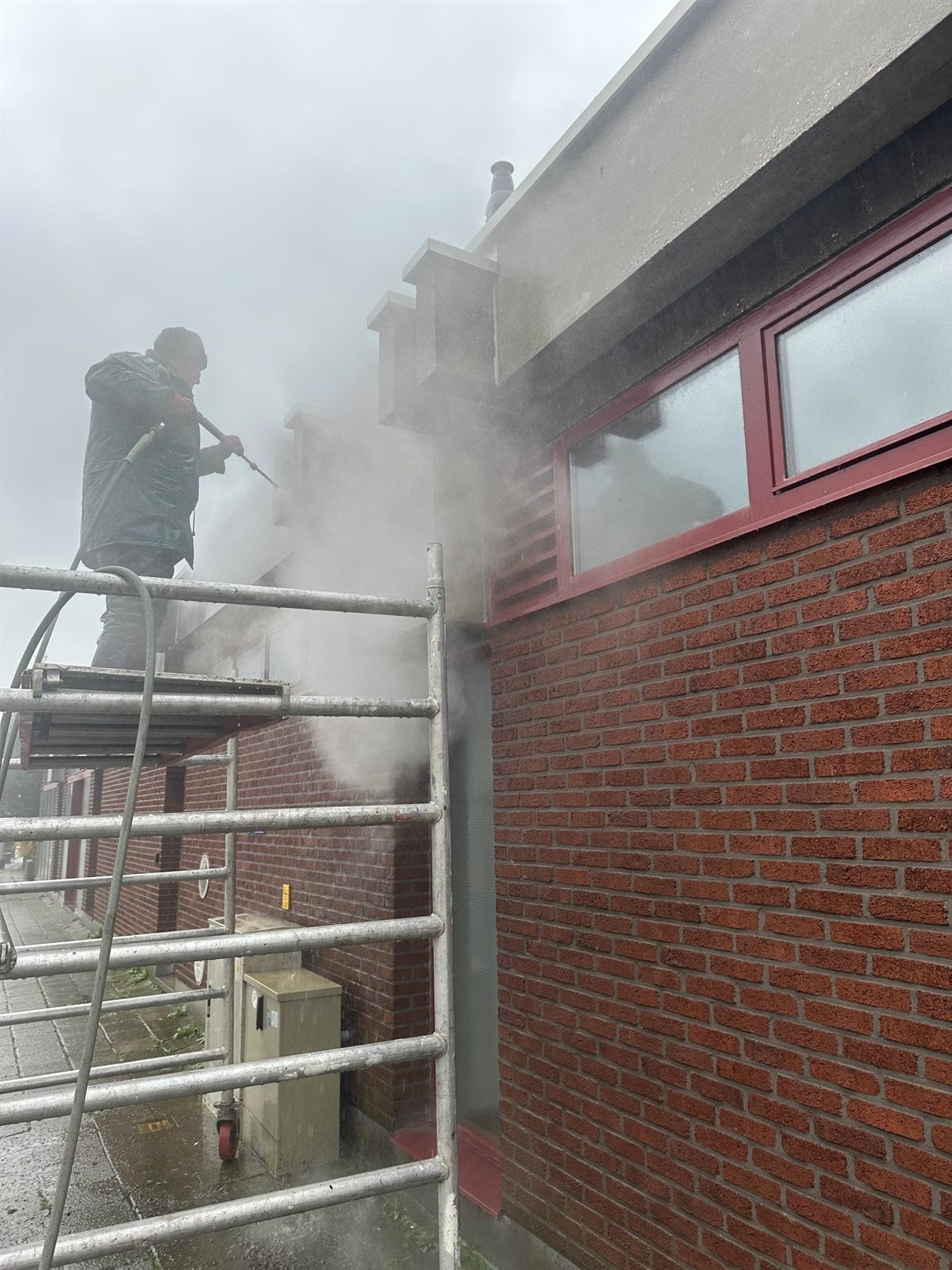 DTRenovatie-vakman reinigt met stoom een gevel, aan het werk vanaf een steiger